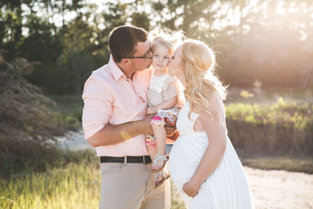 Family shares tender moment together at sunset in an outdoor setting with golden light streaming through trees at Pinckney Island photos.