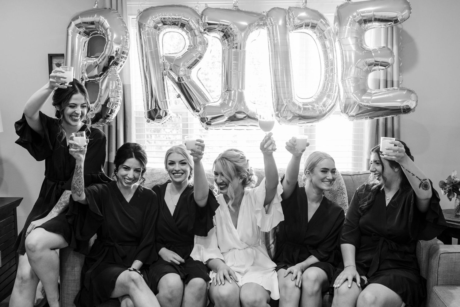 Black and white photo of people celebrating with metallic letter balloons.