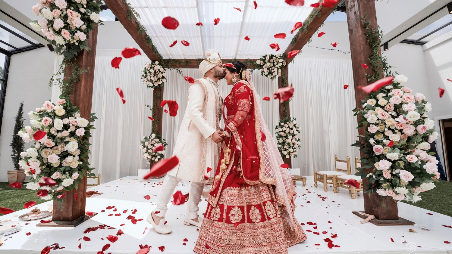 Wedding ceremony setup with red rose petals and floral arrangements creating a romantic pathway.
