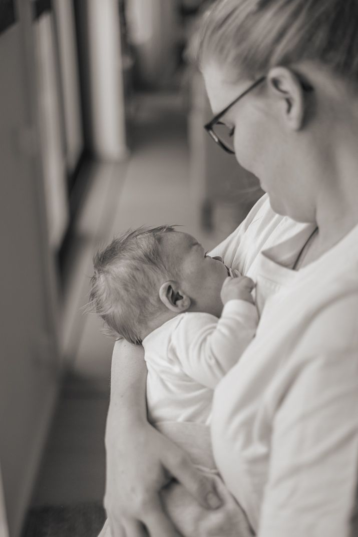 A tender black and white photo of an infant in white clothing being cradled against someone wearing glasses and a white shirt.