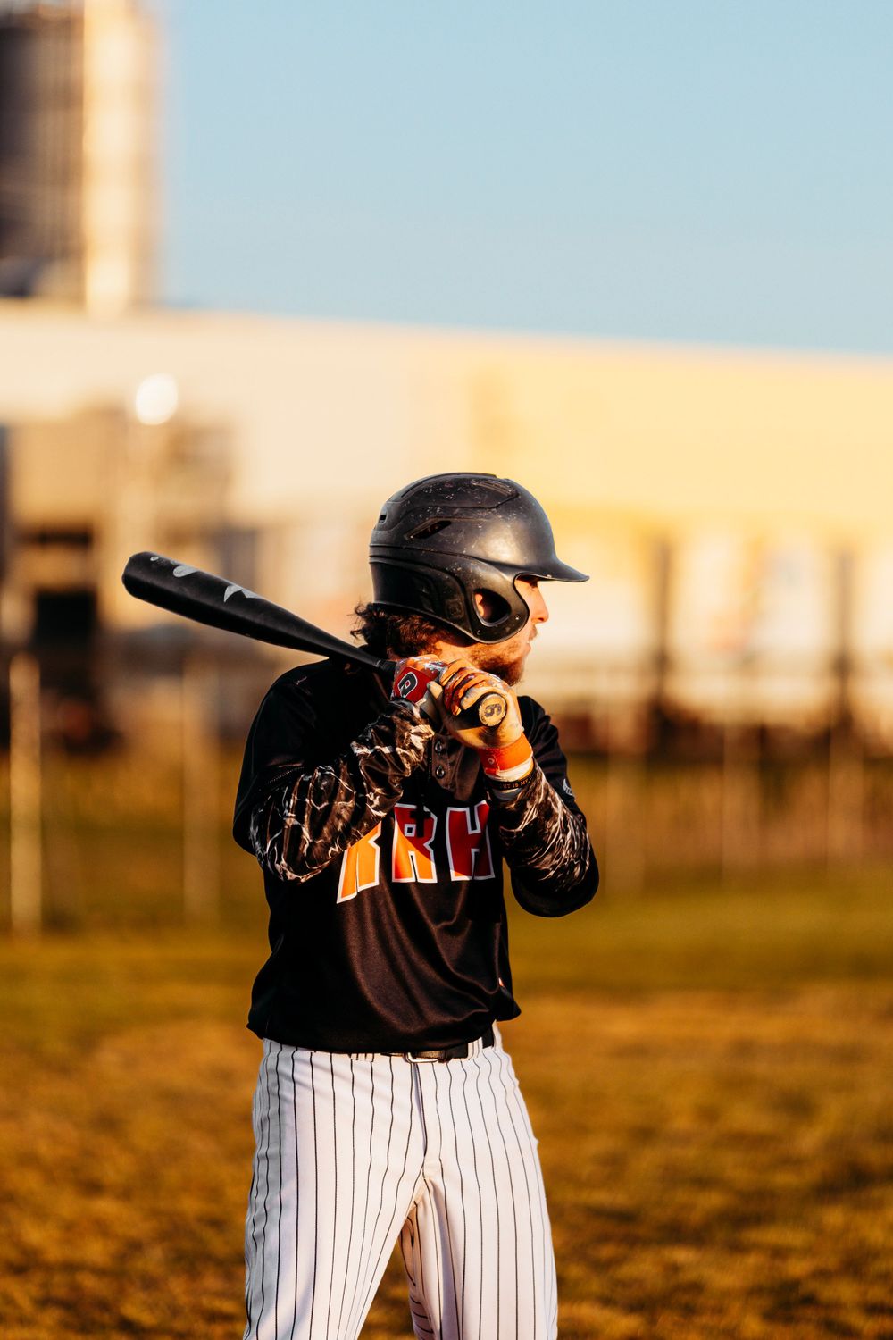 Youth baseball player in black uniform adjusts batting helmet while holding bat at home plate.