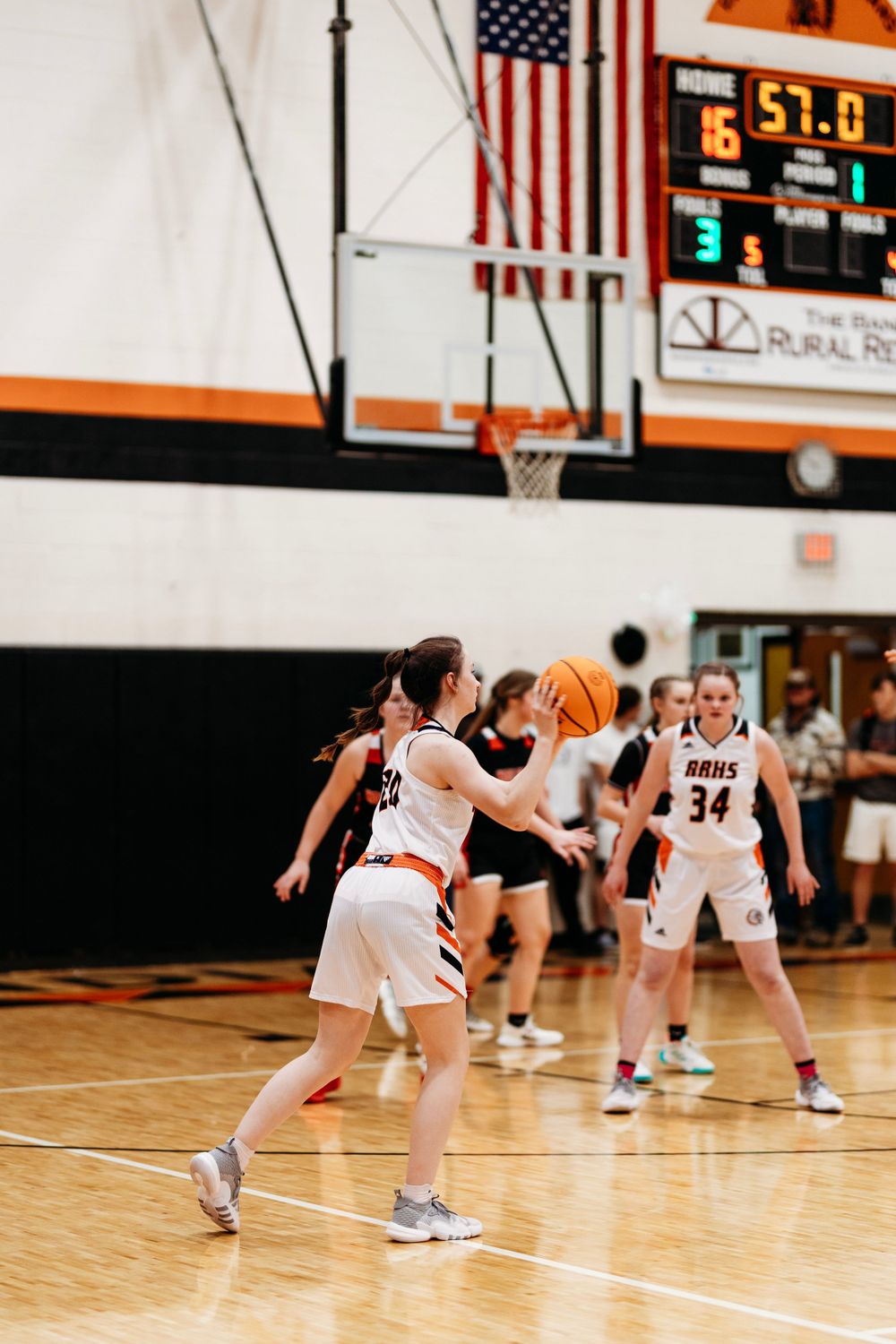 High school girls basketball players compete during a game, with a scoreboard showing 57 points in the background.