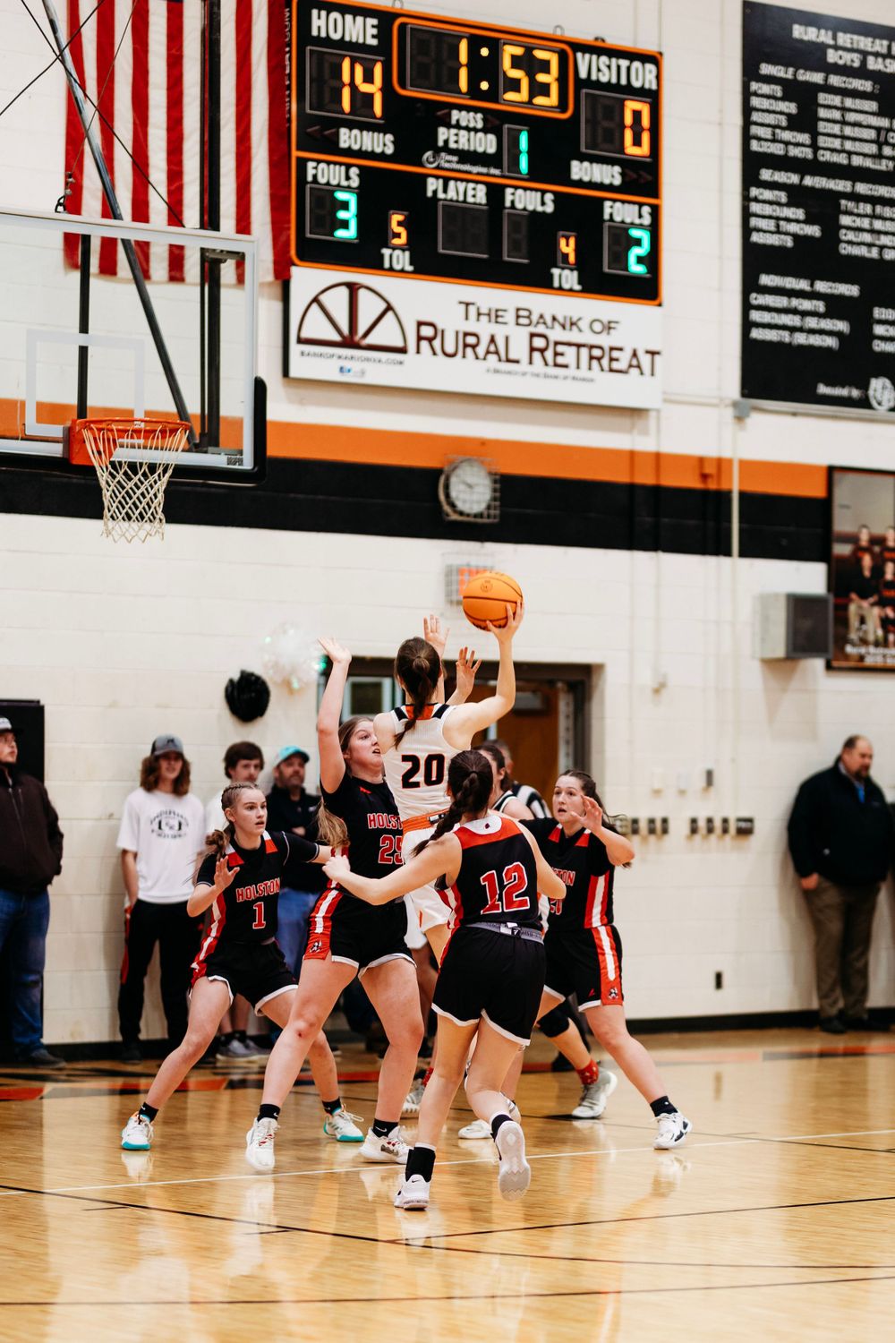 A player in white jersey number 20 attempts a shot while surrounded by defenders during a girls high school basketball game.