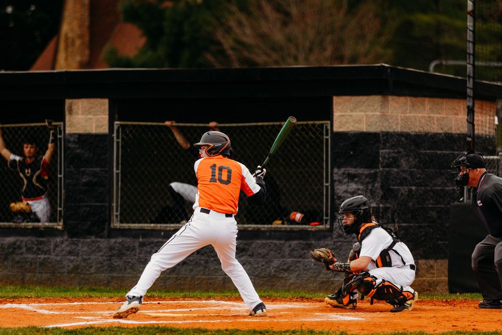 Baseball batter number 10 in orange uniform stands ready at plate while catcher waits behind him.