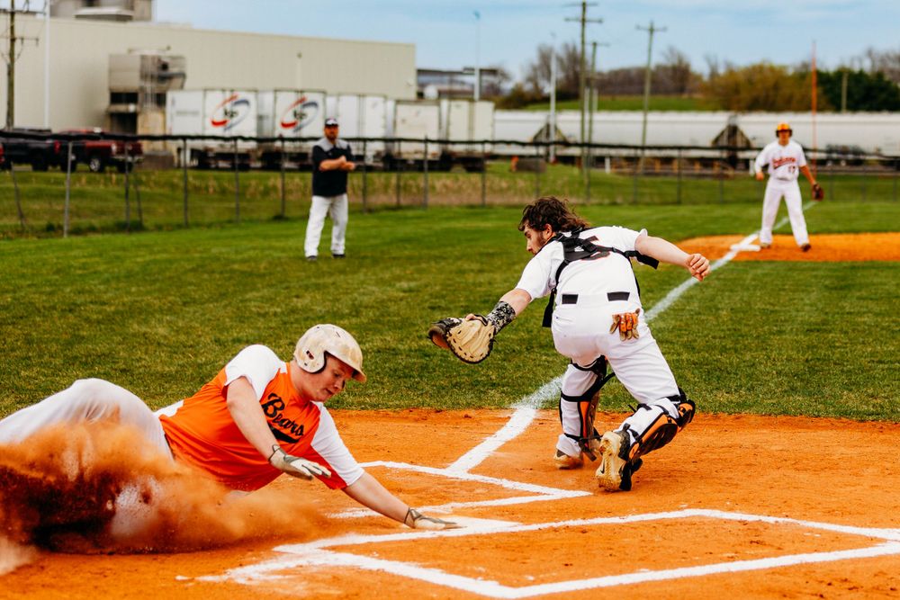 Baseball player in orange slides into home plate as catcher in white attempts a tag during a game.