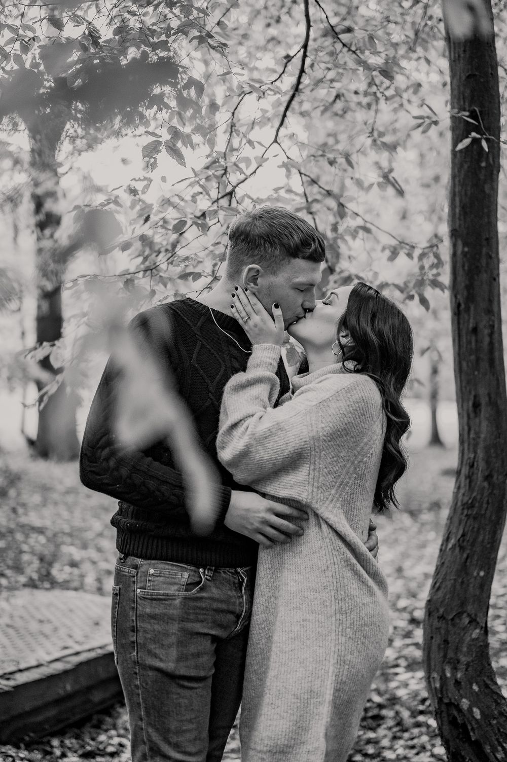 Black and white photo of couple embracing in autumn woods.