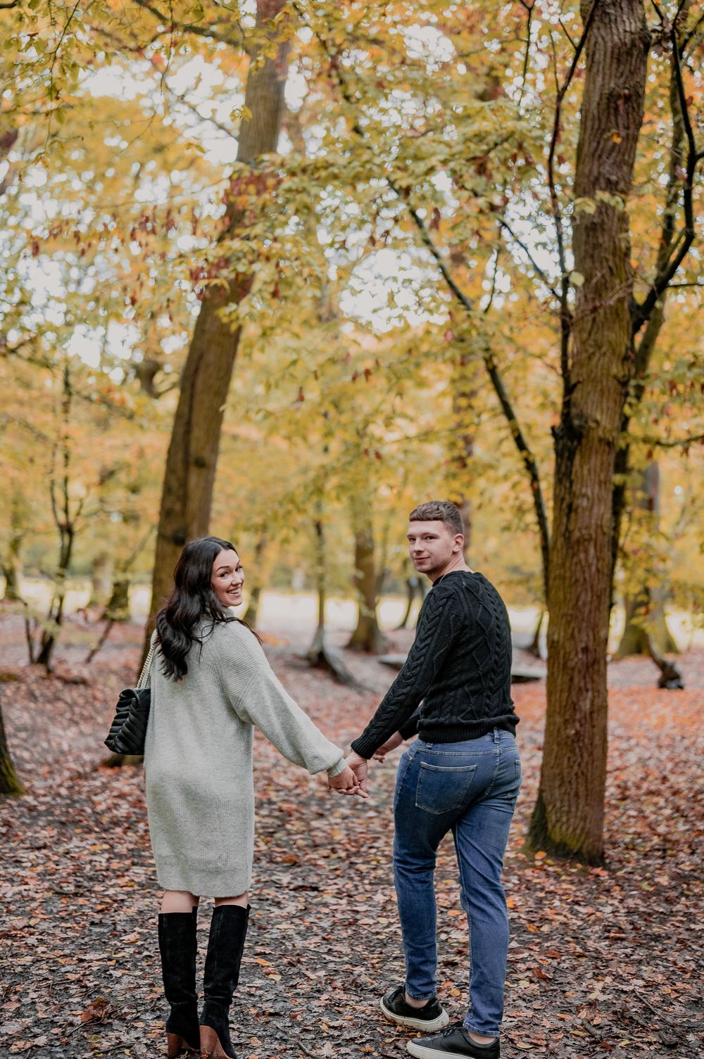 Couple walking hand in hand through autumn forest with fallen leaves.