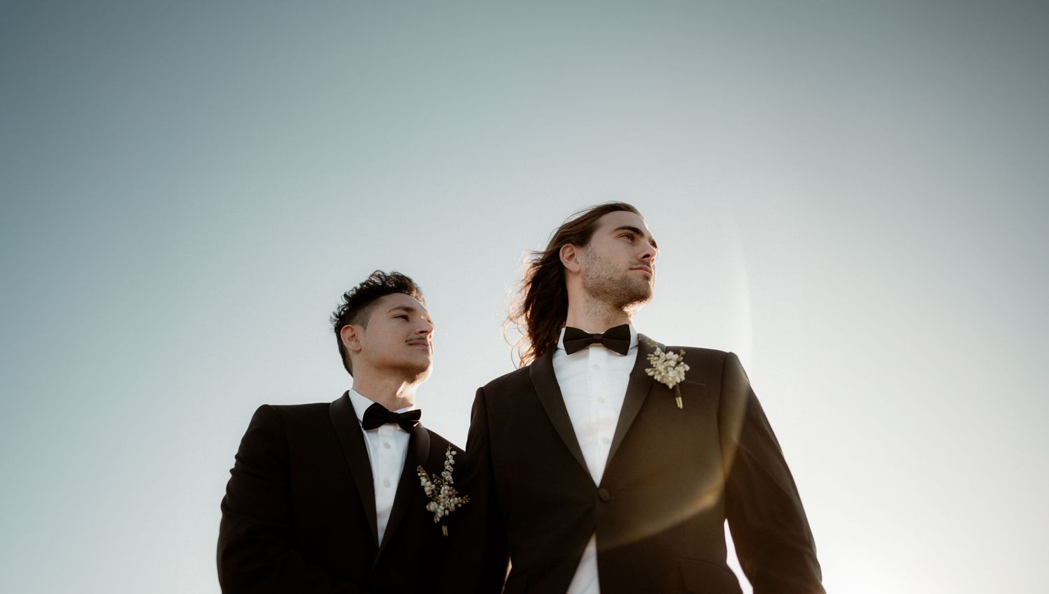 A low shot of two grooms in suits and bow ties looking into the distance.