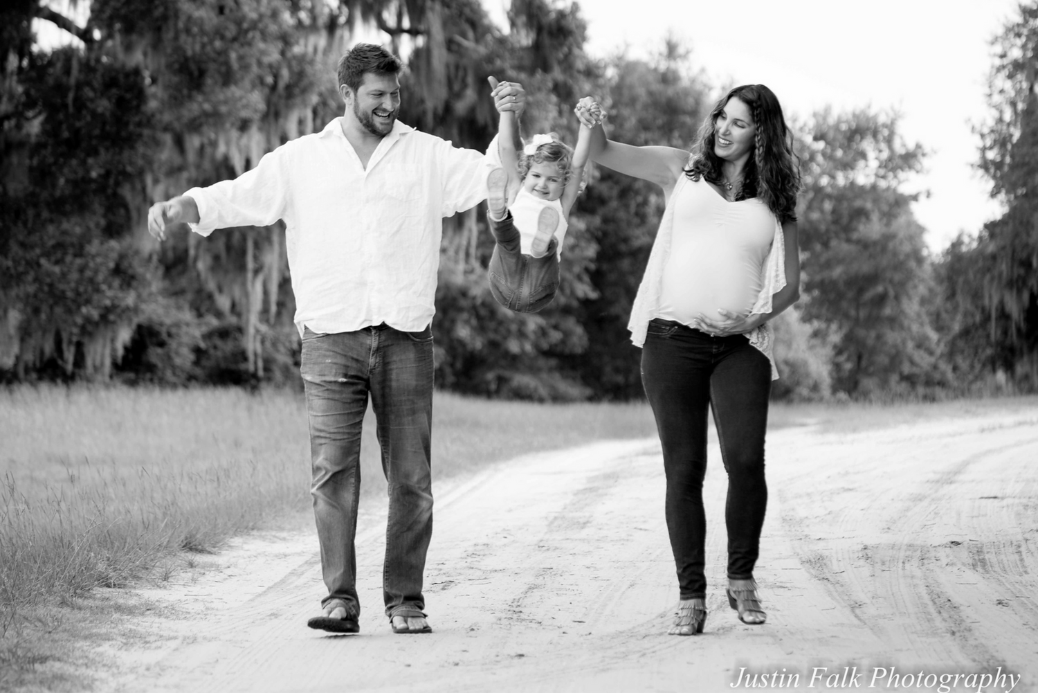 Mom and dad swing toddler by the arms, dirt road