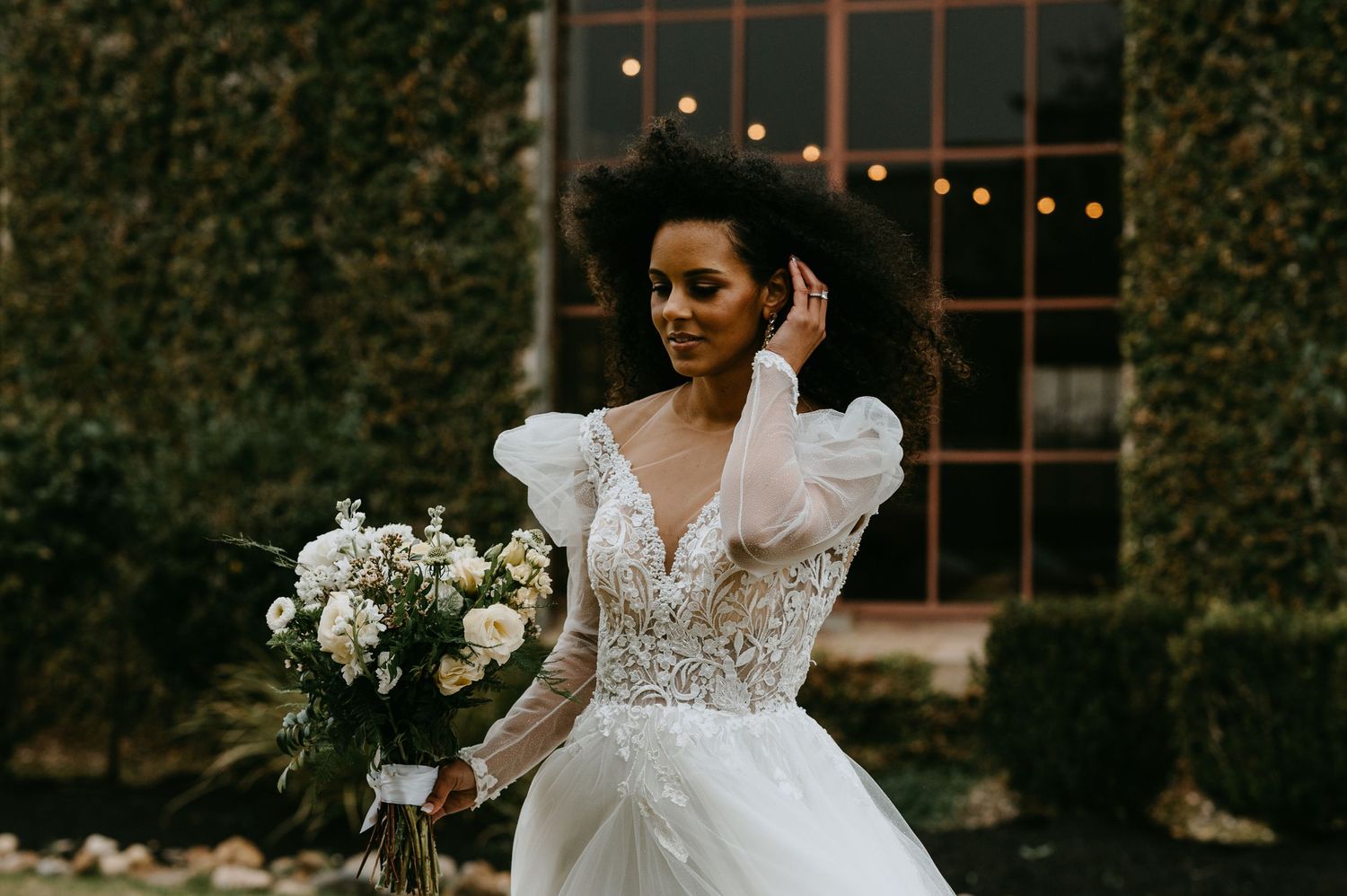 Wedding gown with dramatic puff sleeves and floral bouquet in garden setting.