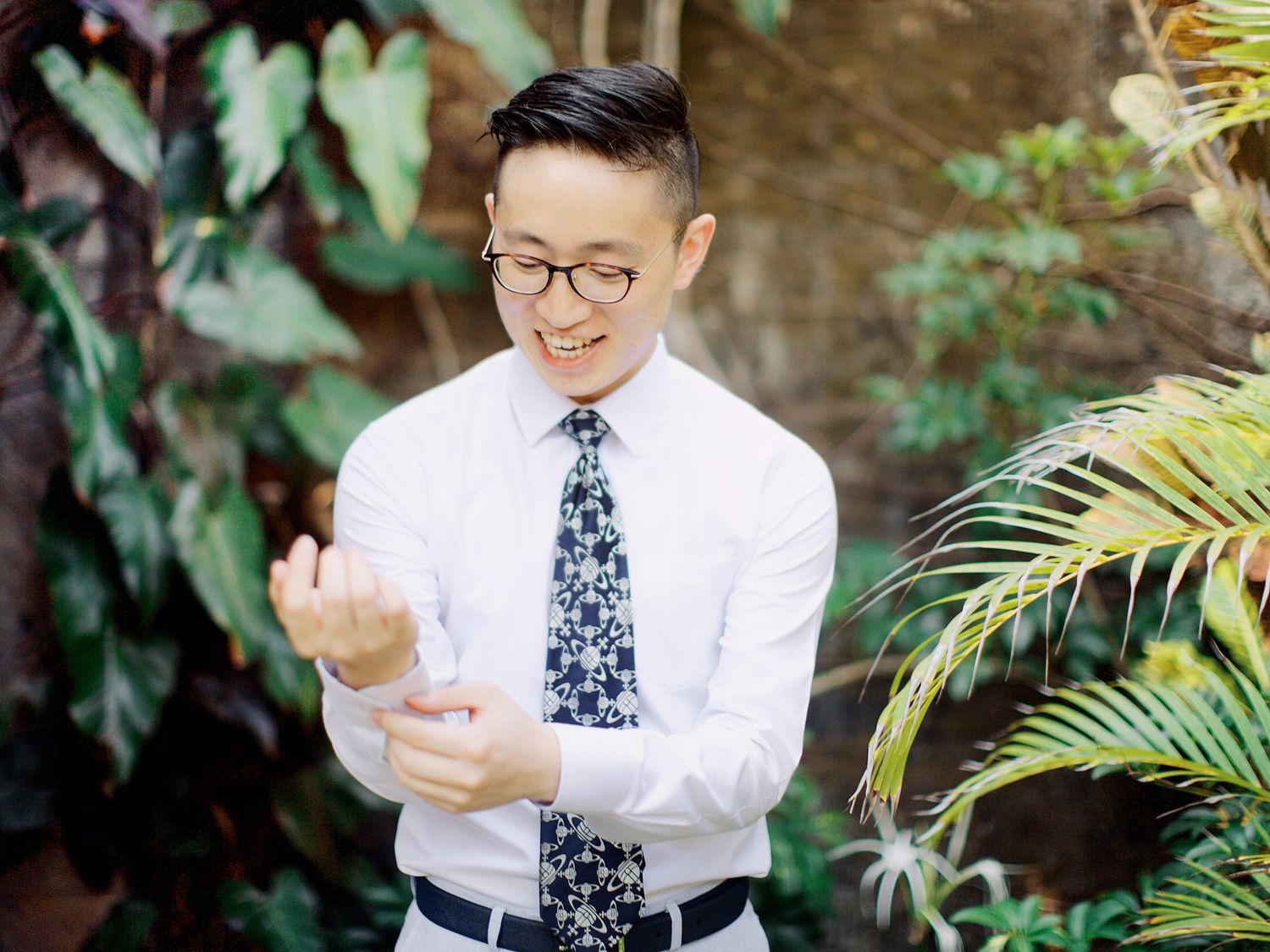 A groom in glasses and a tie adjusting his tie, getting ready at Bulgari Resort Bali.