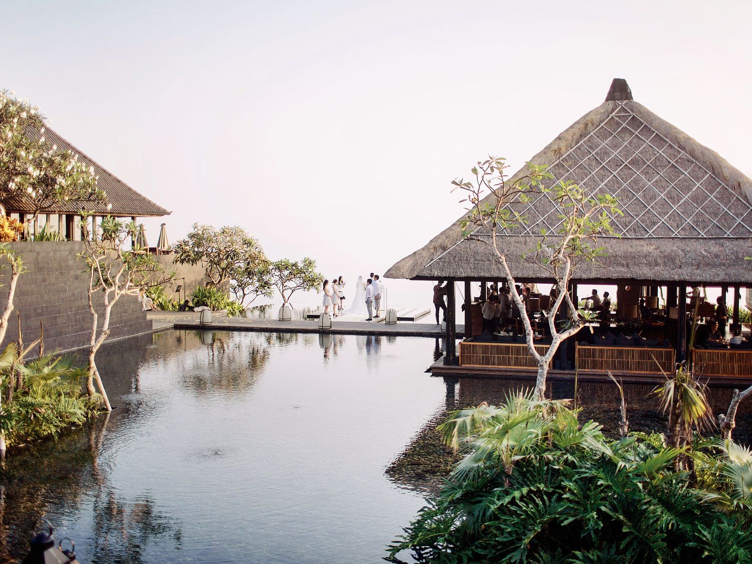 A wedding ceremony at Bulgari Resort Bali, featuring thatched huts and a pool, in a serene resort setting.