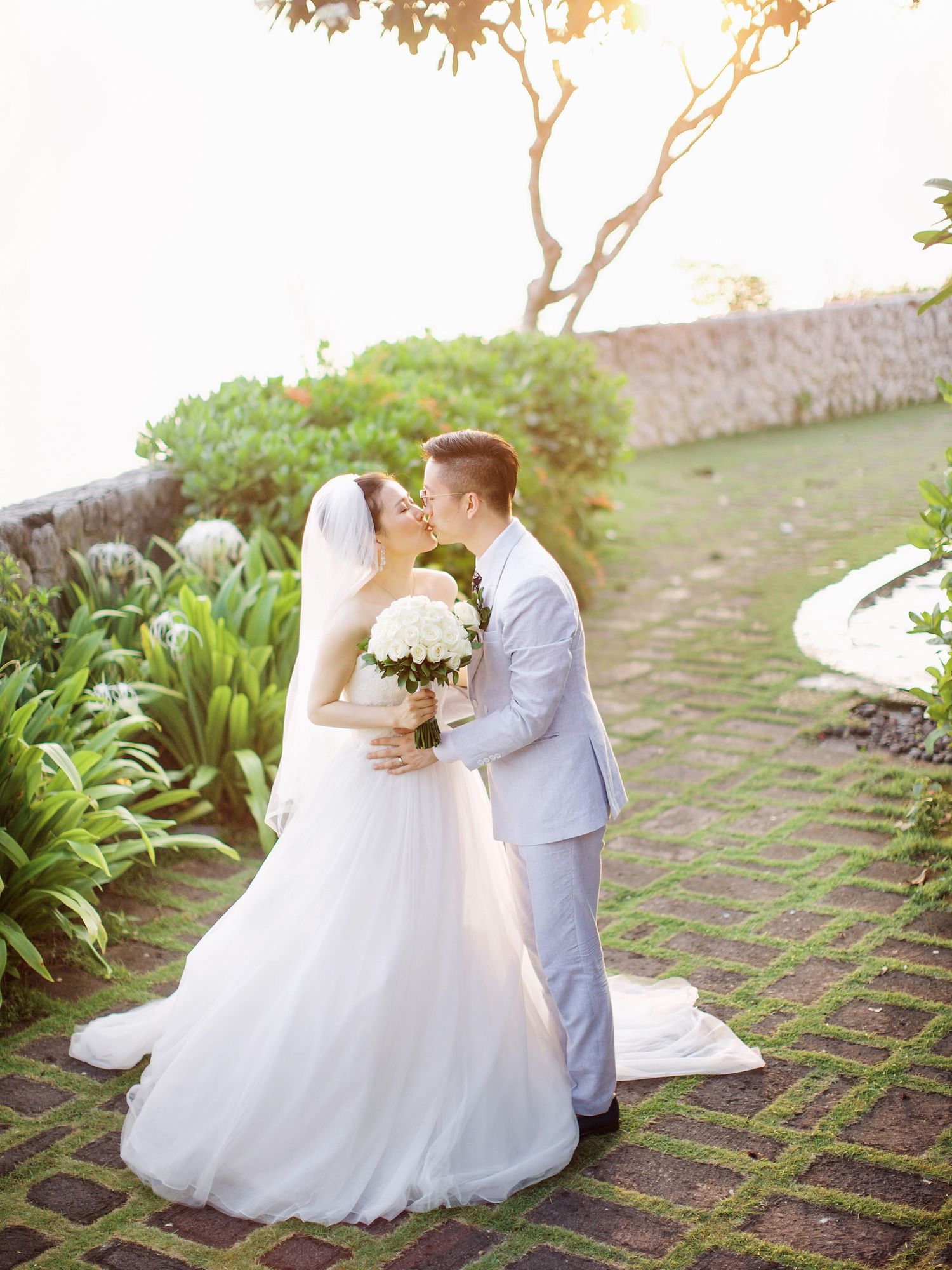 Bride and groom kissing with scenic backdrop of Bulgari Resort Bali.