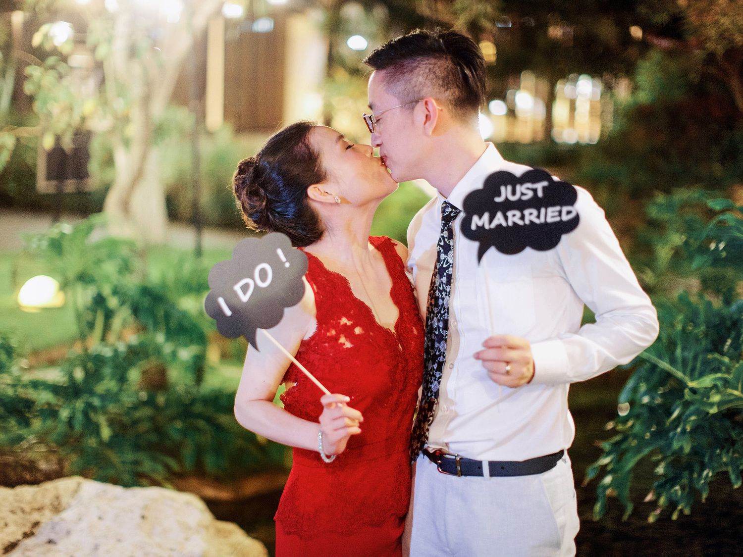 A newlywed couple sharing a romantic kiss, holding "just married" signs, at Bulgari Resort Bali in the evening.