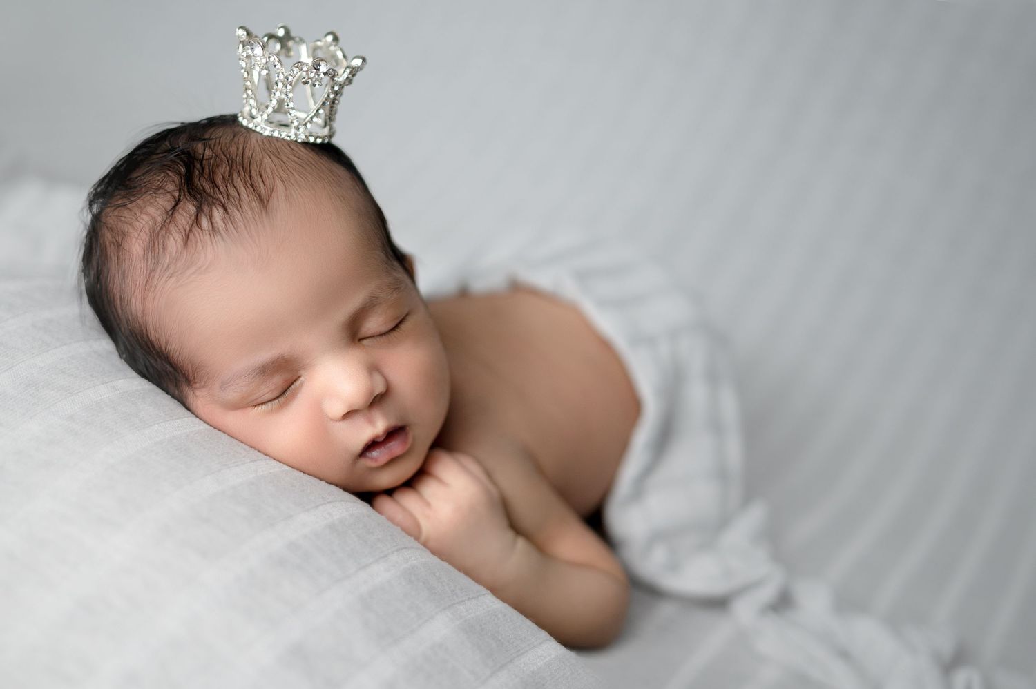 Professional newborn portrait series with baby wearing delicate crown accessory on gray backdrop.