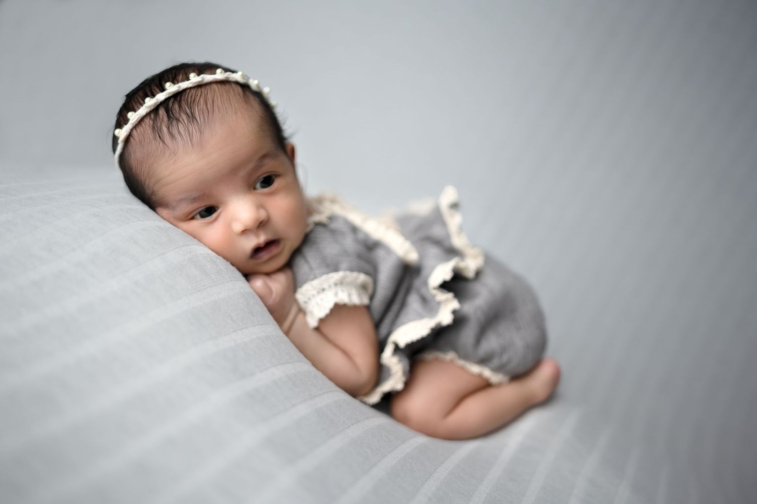Professional newborn portraits with baby wearing white crown and gray wrap against neutral backdrop.