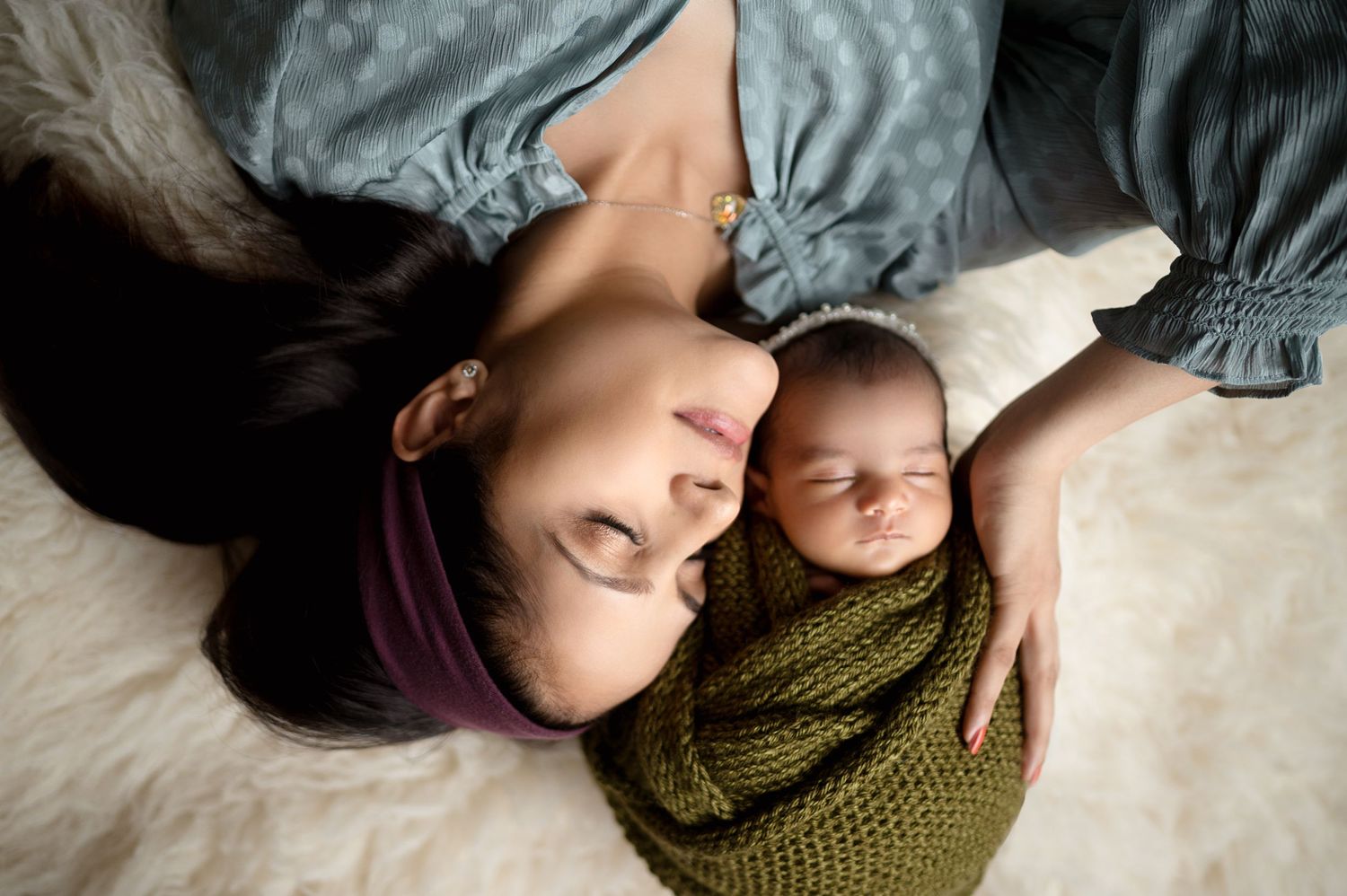 Overhead view of parent and baby in soft blue tones on textured bedding.