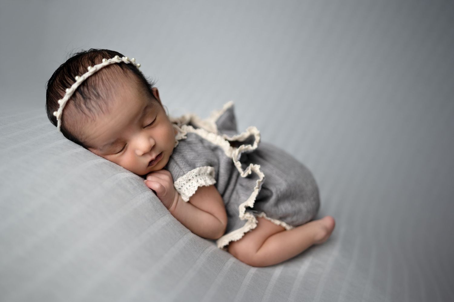 Peaceful newborn in grey wrap sleeping during studio portrait session.