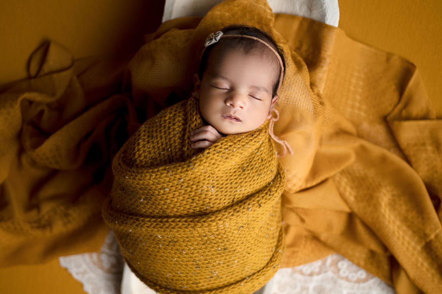 Newborn baby swaddled in warm yellow knitted wrap during artistic portrait session.