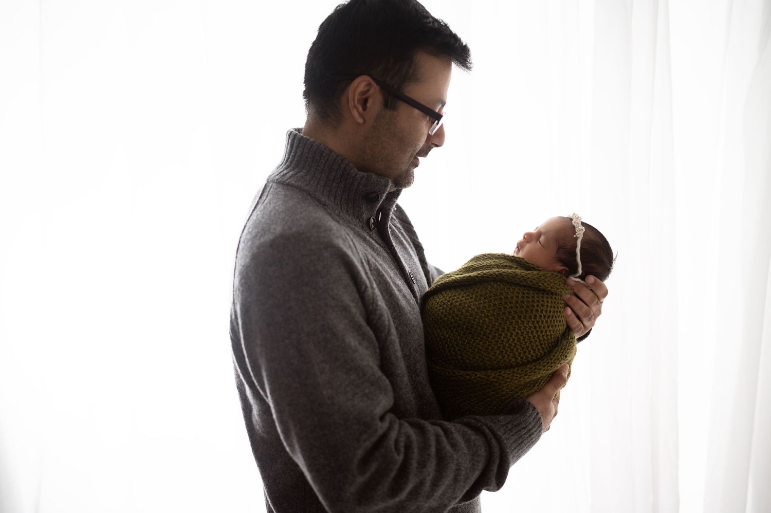 Tender moment between a parent and newborn against a bright window backdrop.