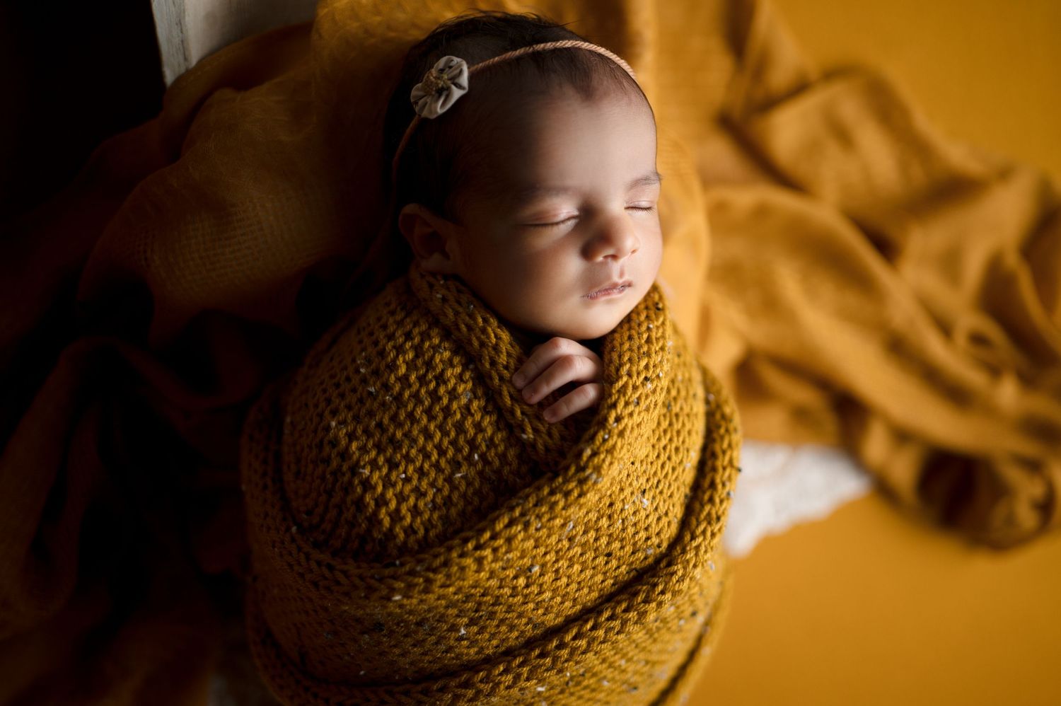 Baby sleeping peacefully in golden knit wrap with warm ambient lighting.