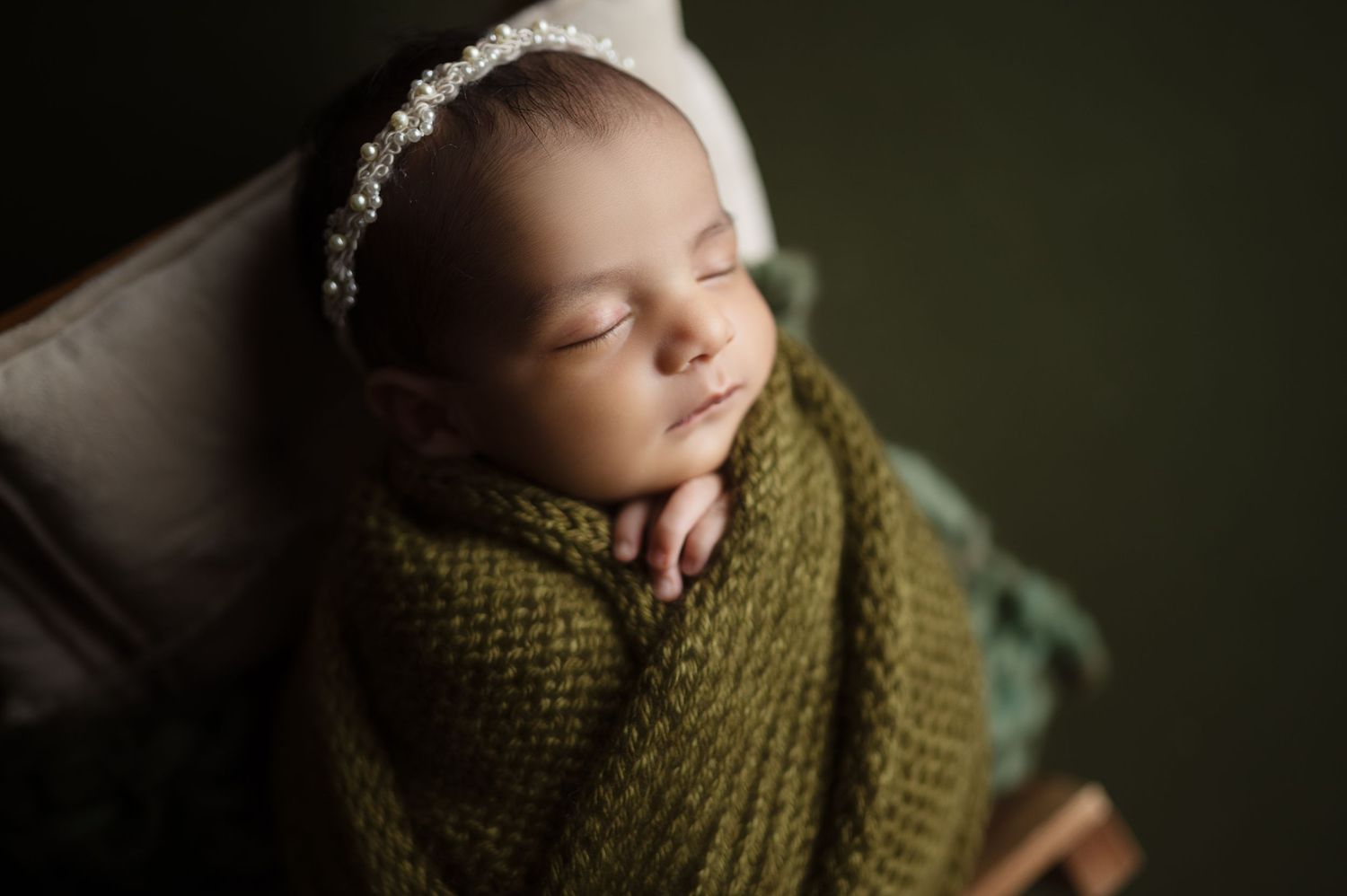 Sleeping baby wrapped in green knit blanket during professional portrait session.