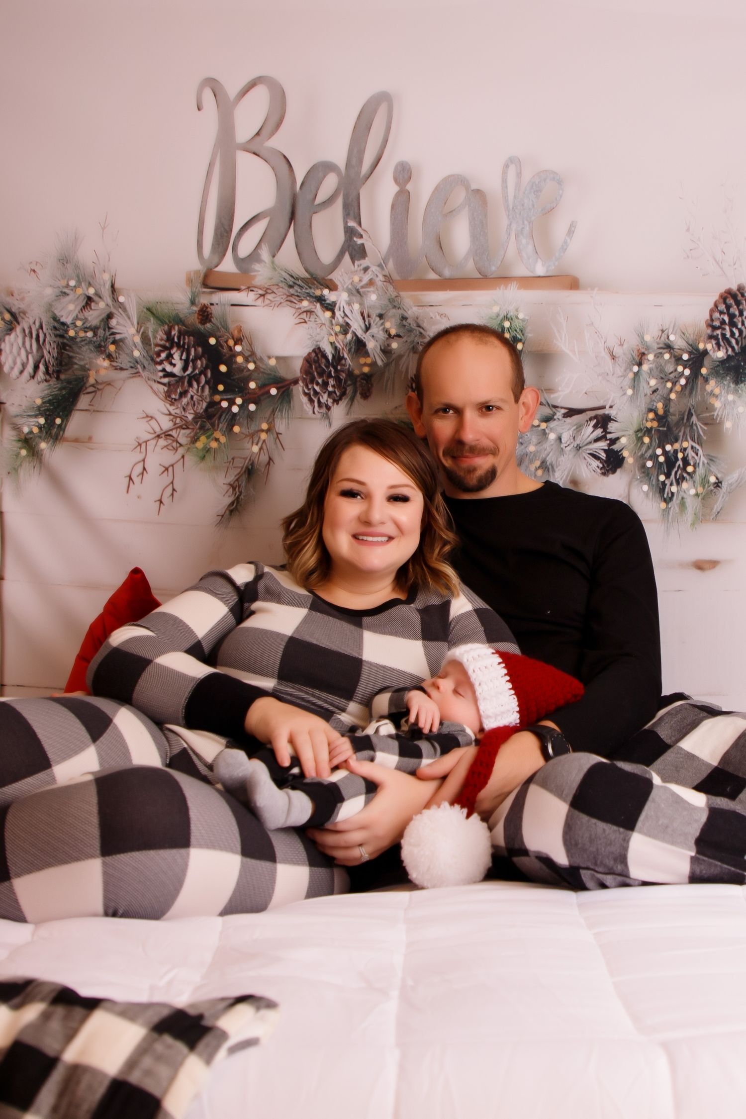 Cozy winter family photo with buffalo plaid blankets and festive Believe sign and garland decor.
