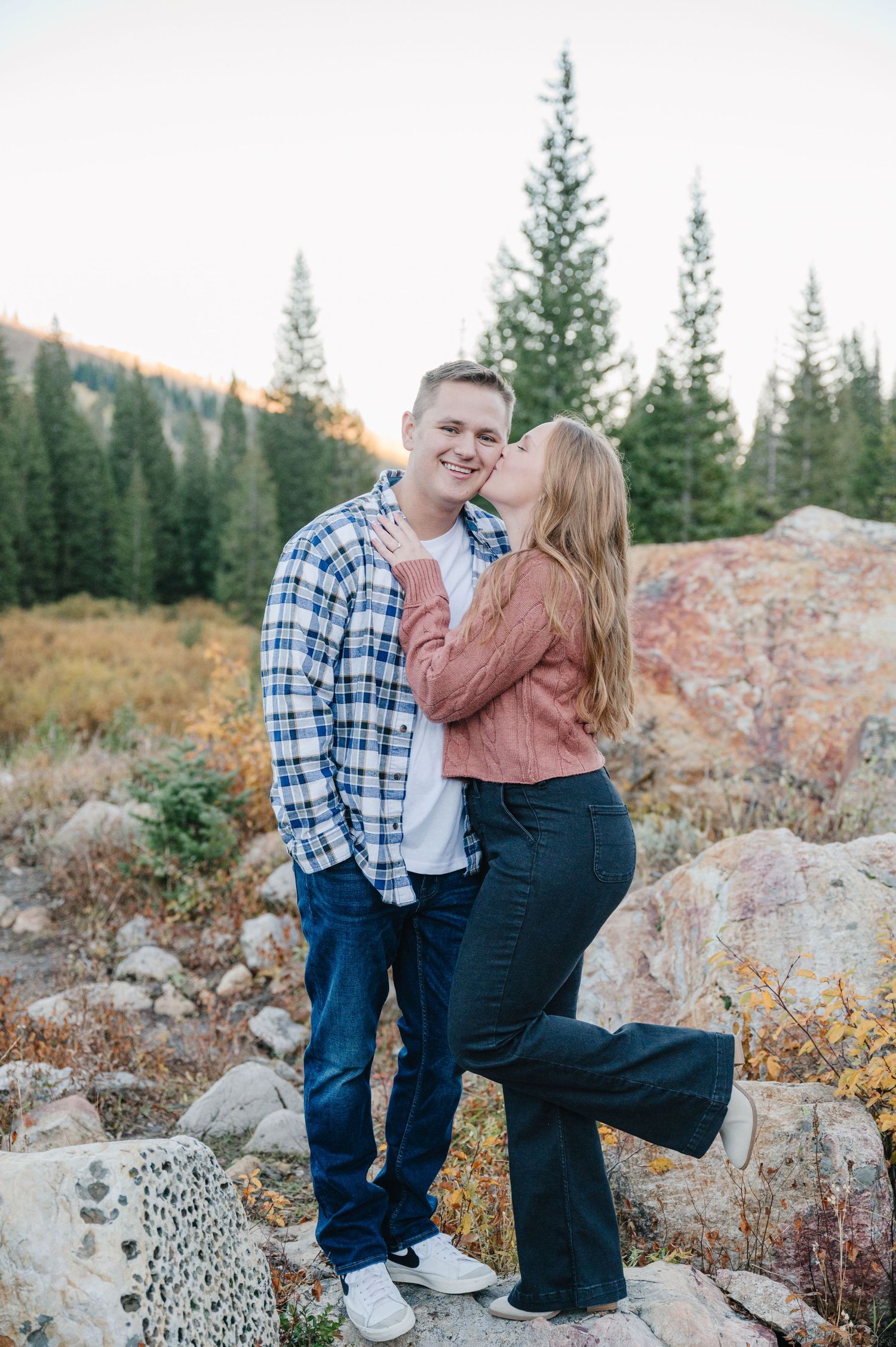 Couple sharing an intimate moment on rocky terrain with evergreen forest backdrop.