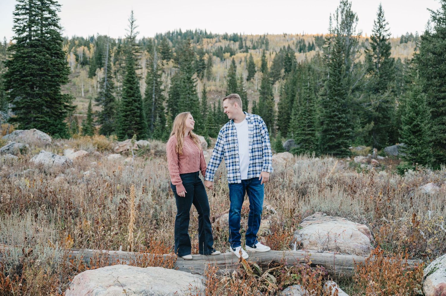 Couple standing on rocky terrain with autumn mountain landscape in background.