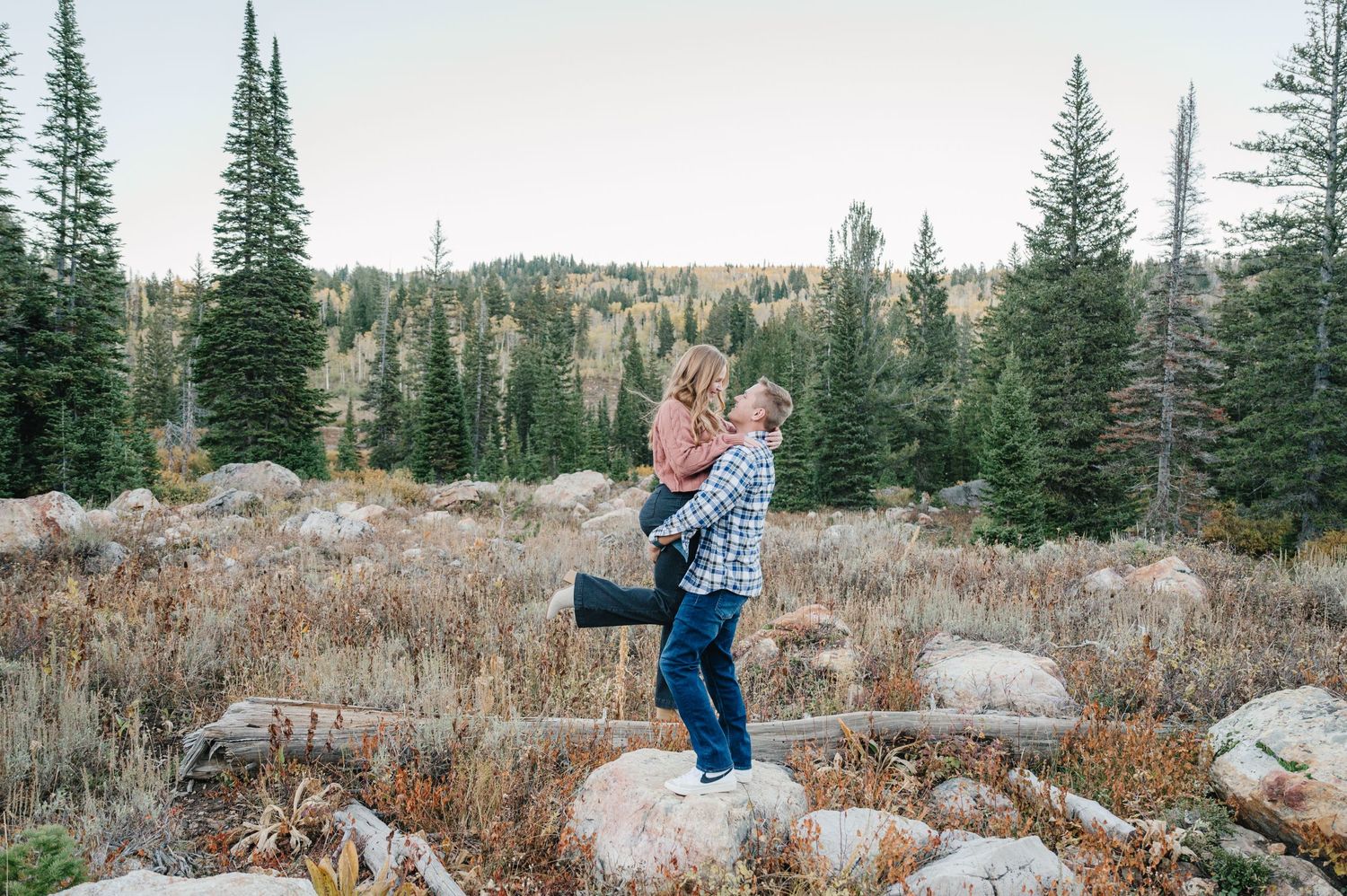 Playful moment between couple on rocky mountain terrain surrounded by pine trees.