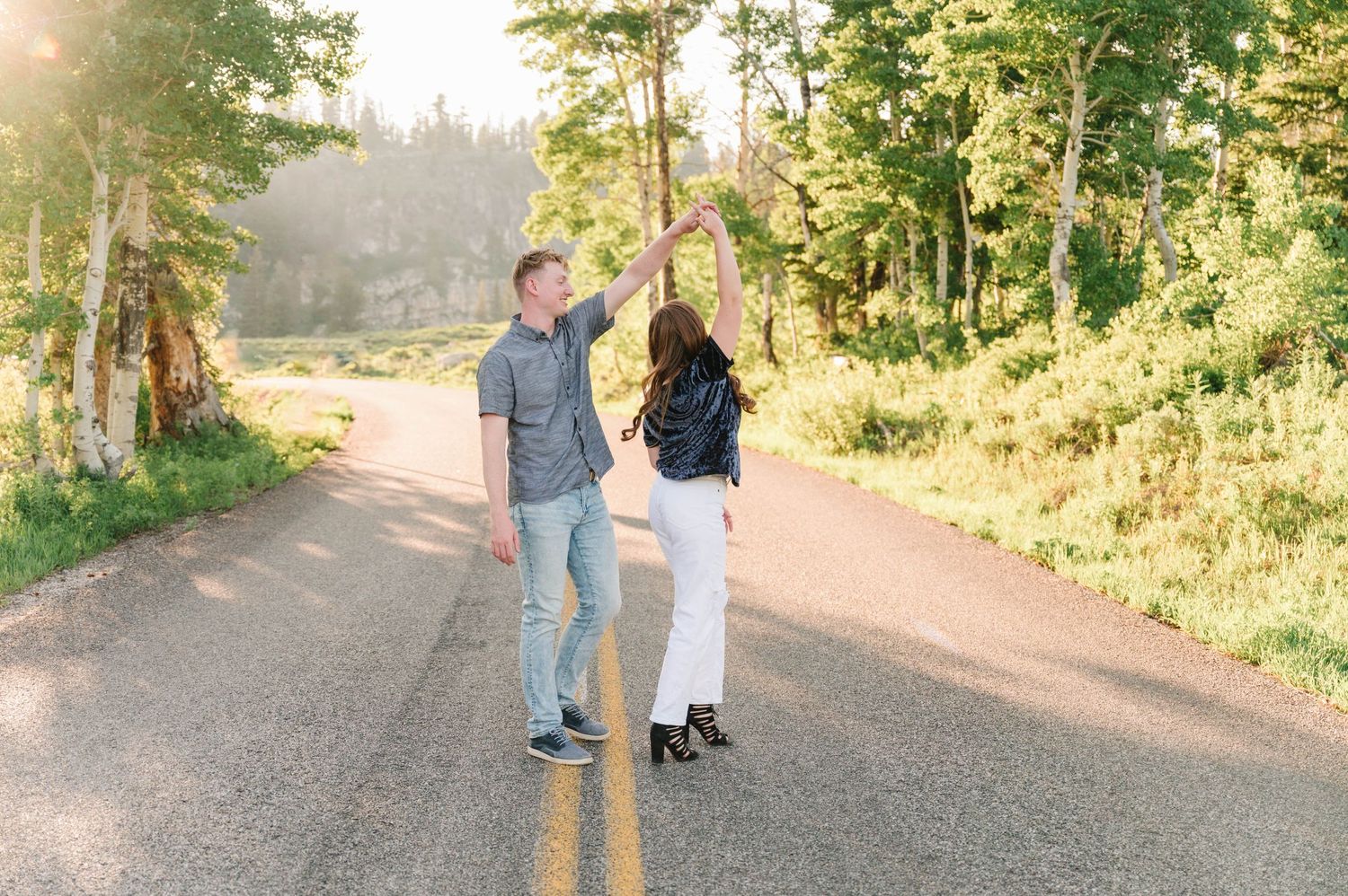 Joyful couple dancing together on a tree-lined country road.