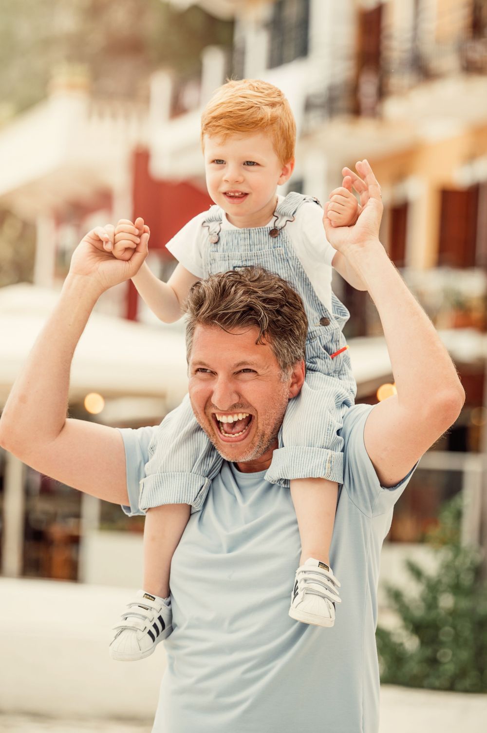 Playful moment with child riding on shoulders against colorful Mediterranean buildings.
