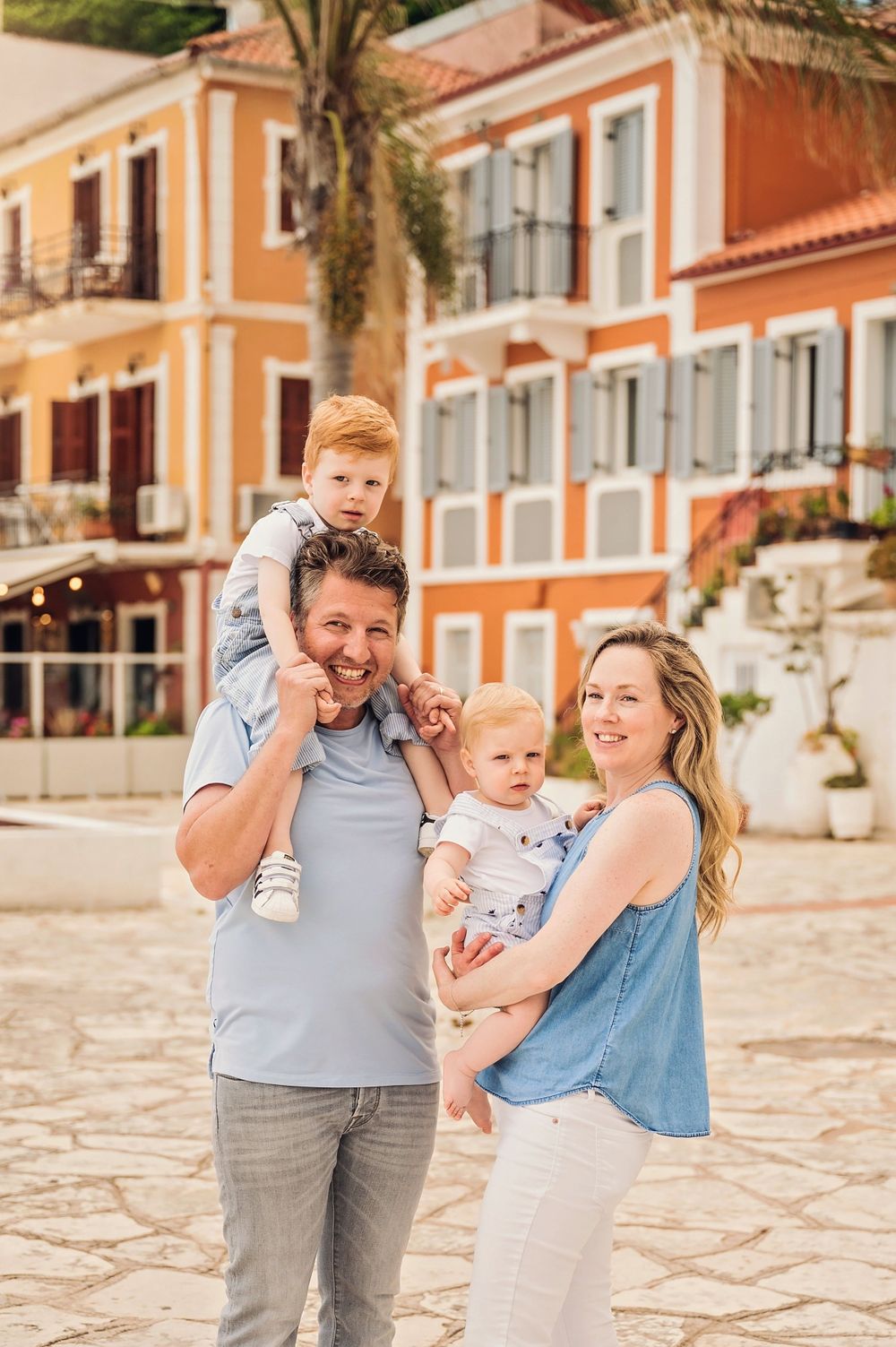 Family portrait outdoors with Mediterranean architecture featuring orange buildings and palm trees.