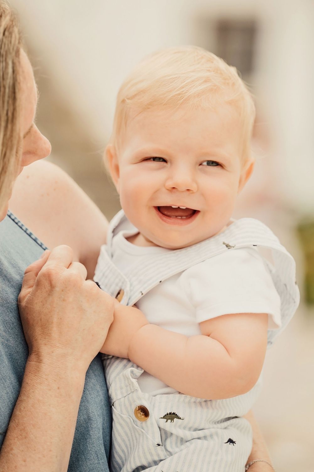 Smiling baby in white outfit being held close while laughing.
