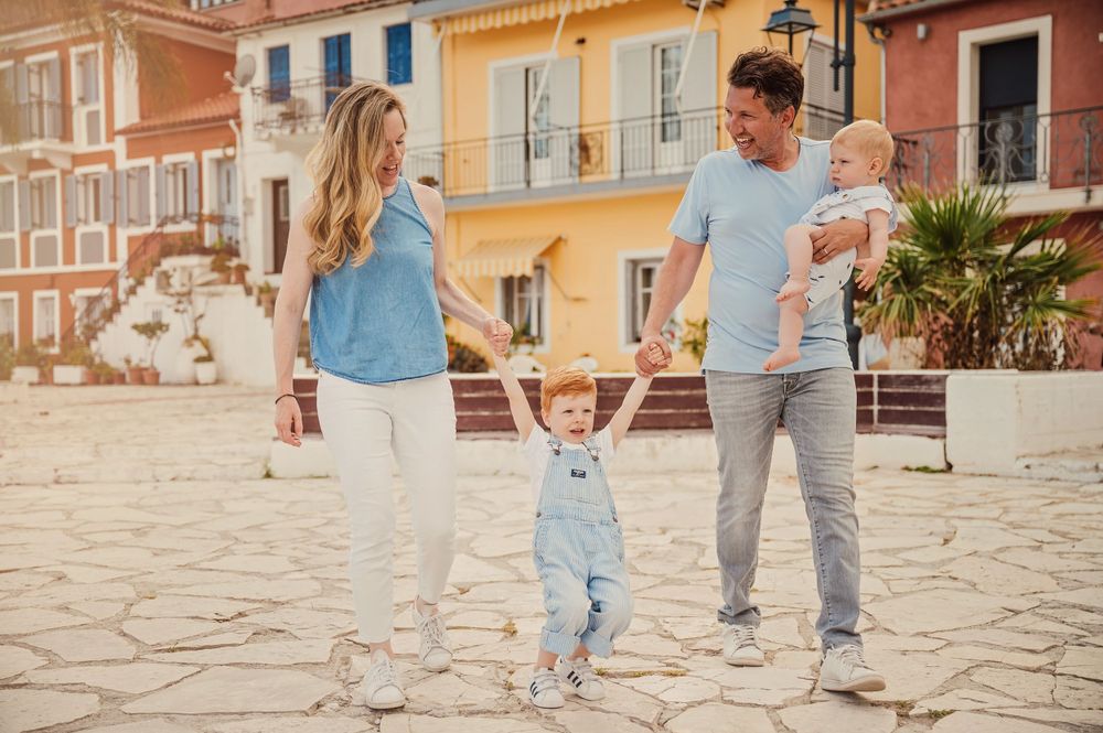 Family having fun walking on cobblestone plaza with colorful buildings in background.