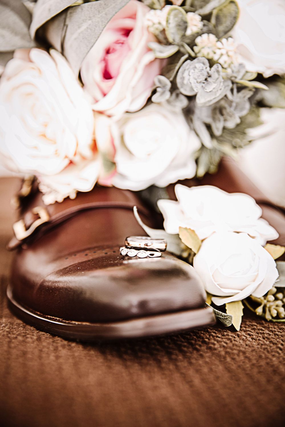 Wedding rings nestled among delicate pink and white roses on a textured brown surface.