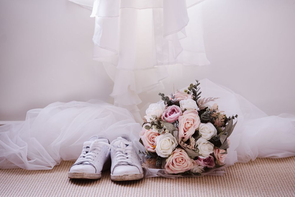 White wedding dress, shoes, and pink floral bouquet arranged on light carpet.