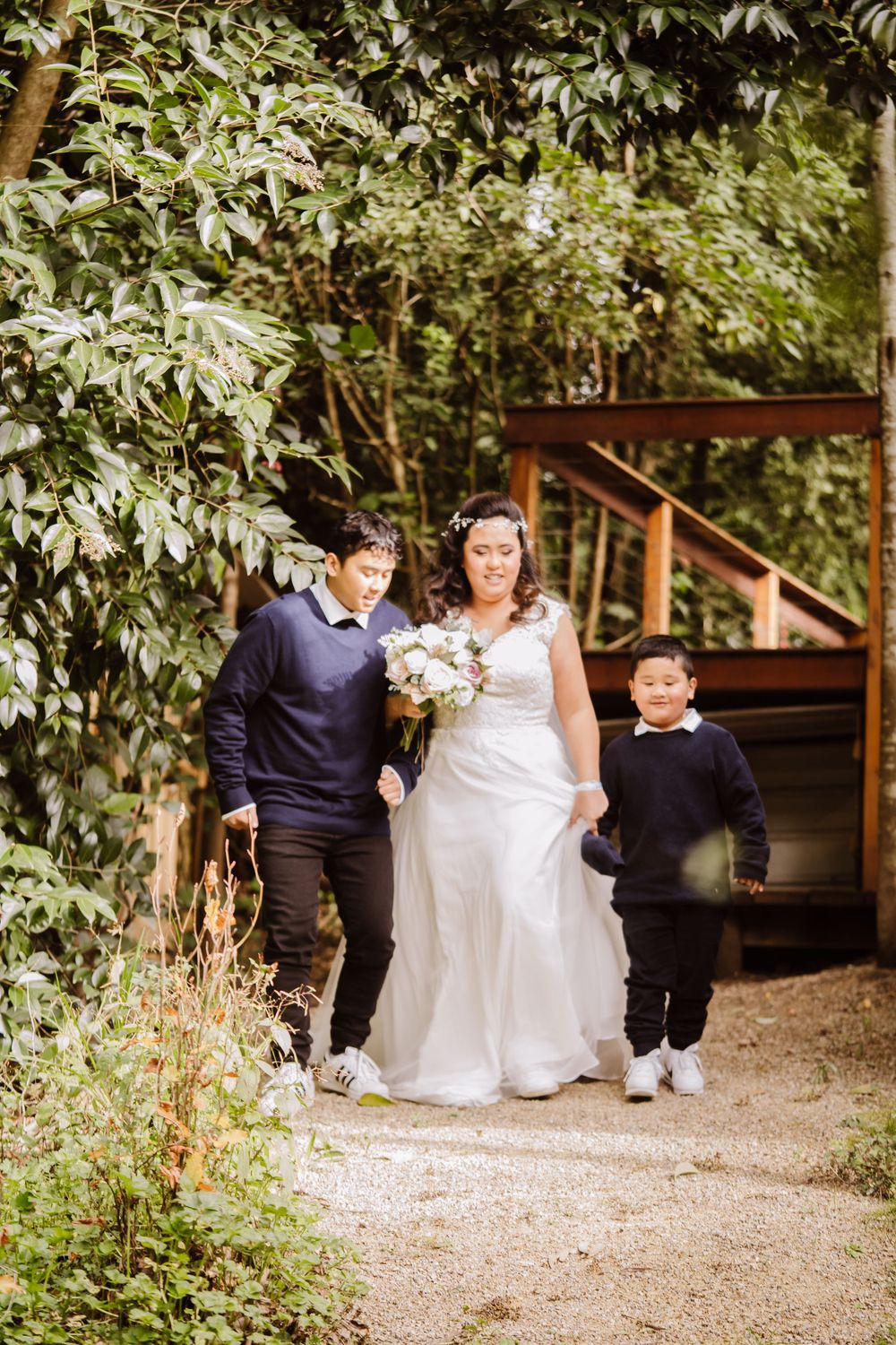 Wedding party walking along garden pathway surrounded by lush greenery.