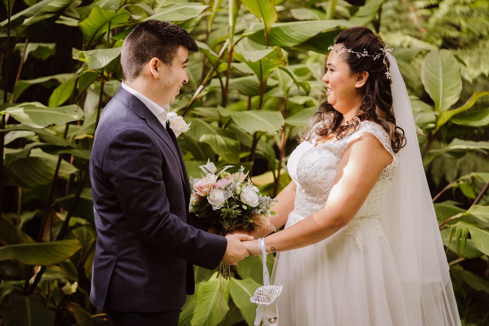 Couple shares intimate moment surrounded by green foliage during outdoor wedding ceremony.