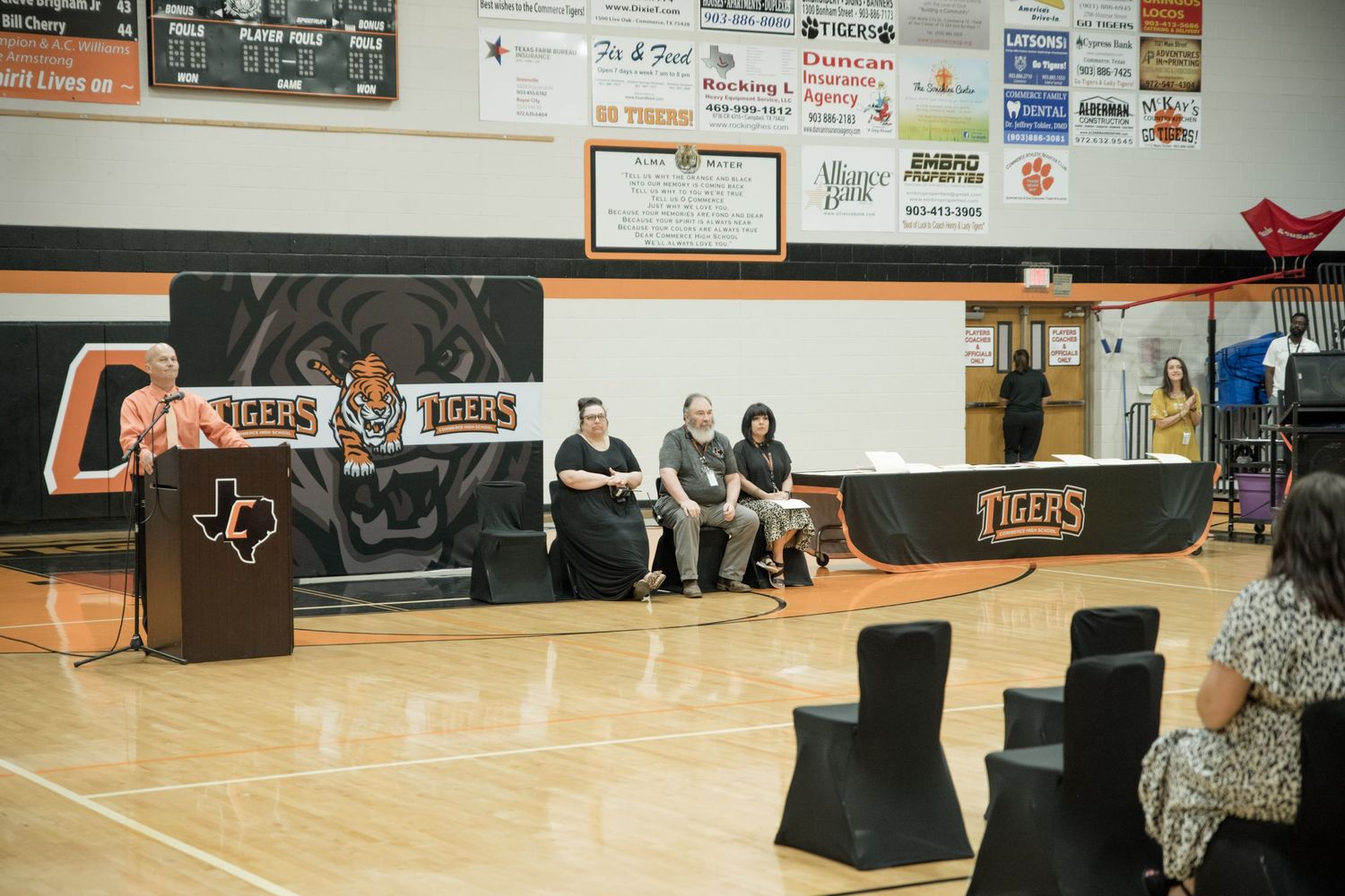 School gymnasium with team logo and sponsor banners displayed on wall.