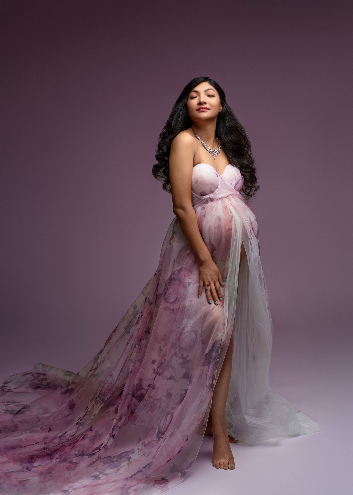 a woman poses for maternity photos in a flowery purple dress