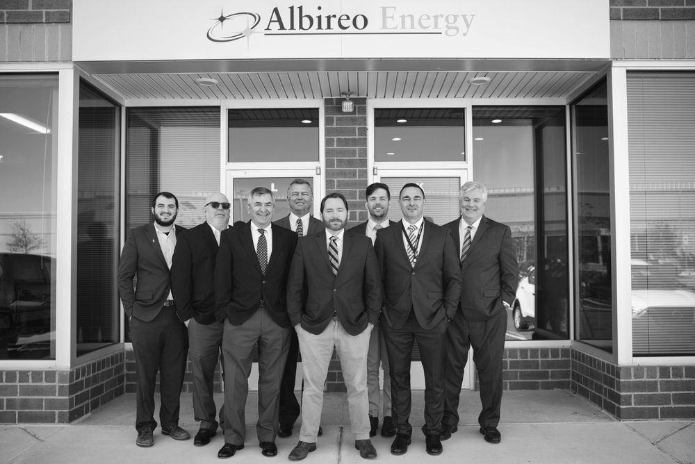 Group photo of seven professionals in business attire standing outside Albireo Energy office entrance.