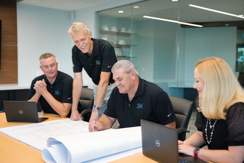 Team meeting with four professionals reviewing blueprints and documents at a modern office table.