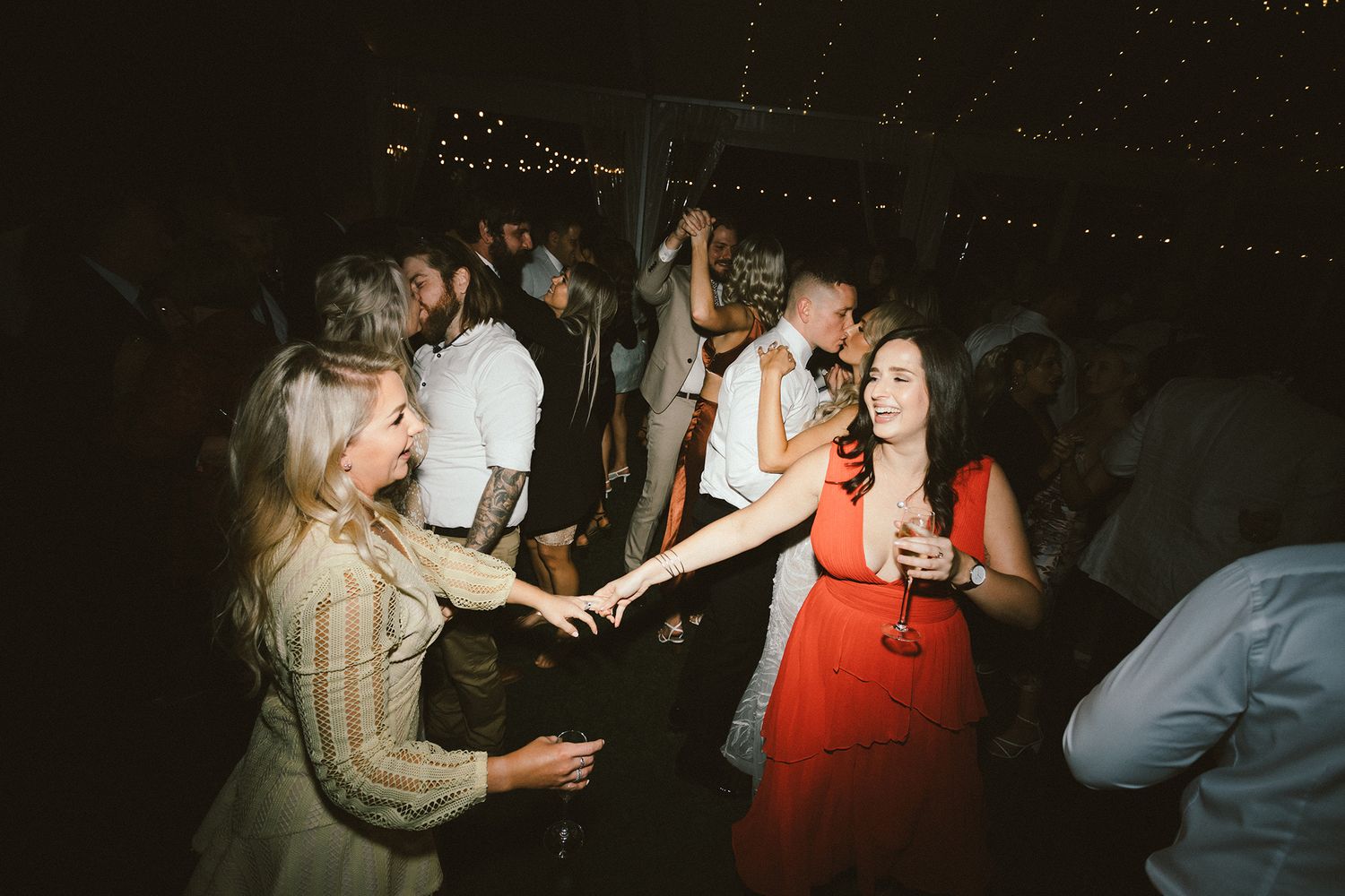 Guests dancing and mingling at a nighttime wedding reception under stringed lighting.