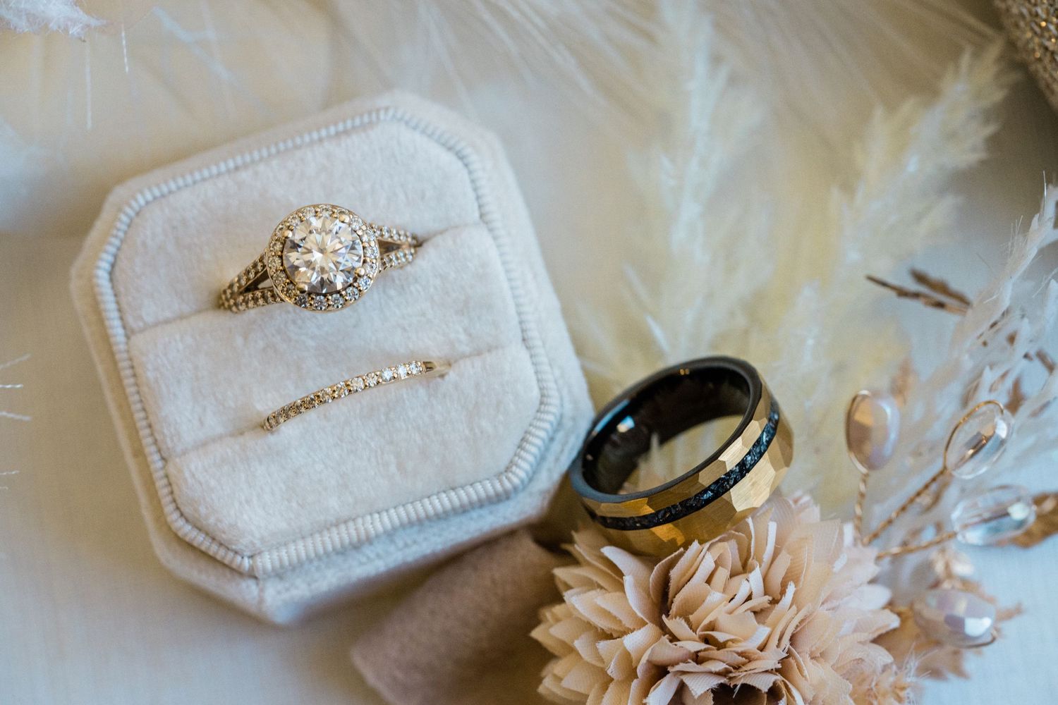 Wedding rings and engagement ring displayed in a white velvet box with dried flowers.