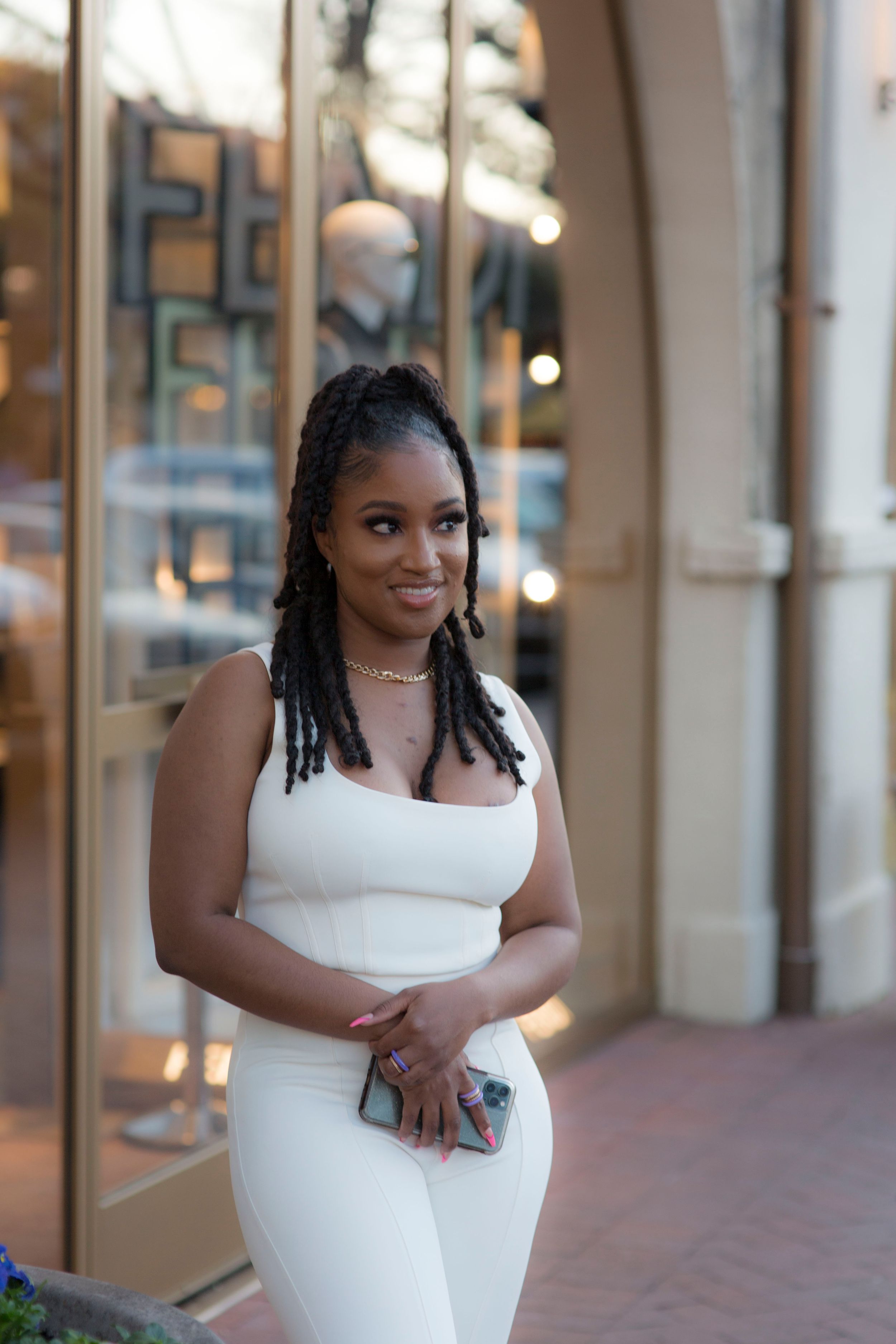 Urban photoshoot in white dress along storefront windows with evening lighting.