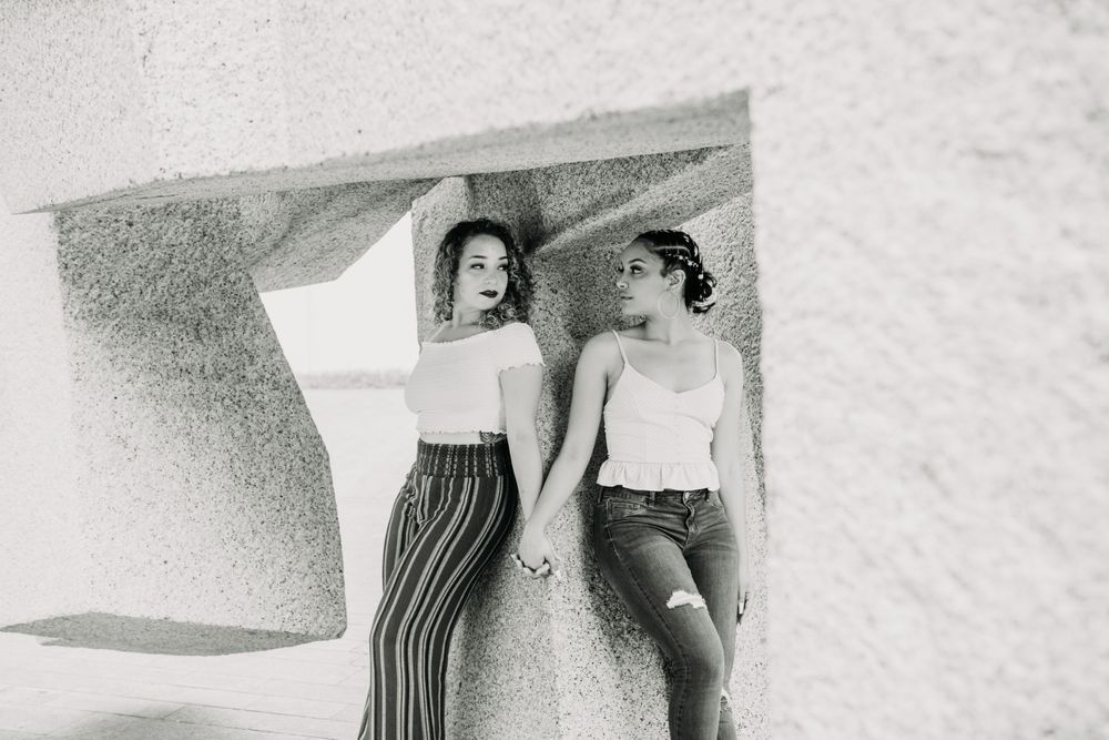 A vintage black and white photo of two people leaning against a wall while holding hands.