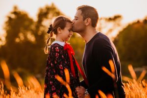 Two people sharing a tender moment in a field at sunset with golden light filtering through tall grass.