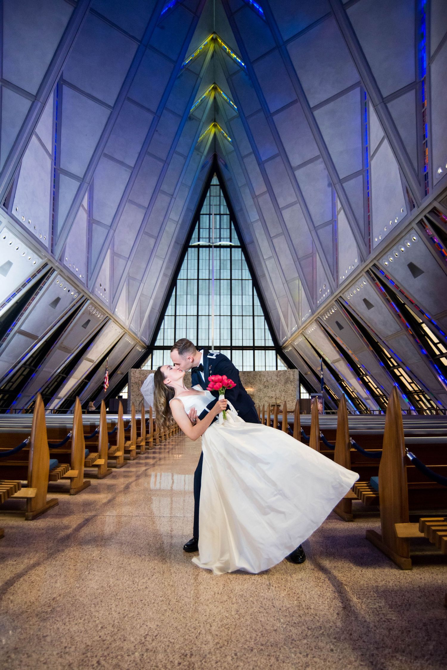 A dramatic wedding photo in a modern chapel with vaulted ceilings and blue lighting.