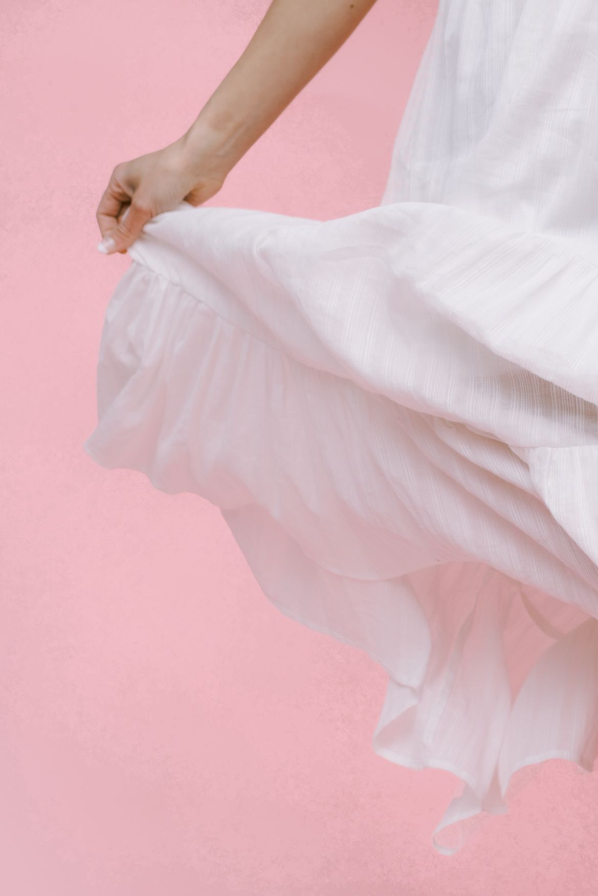Close-up of white ruffled dress fabric flowing against a pink background.